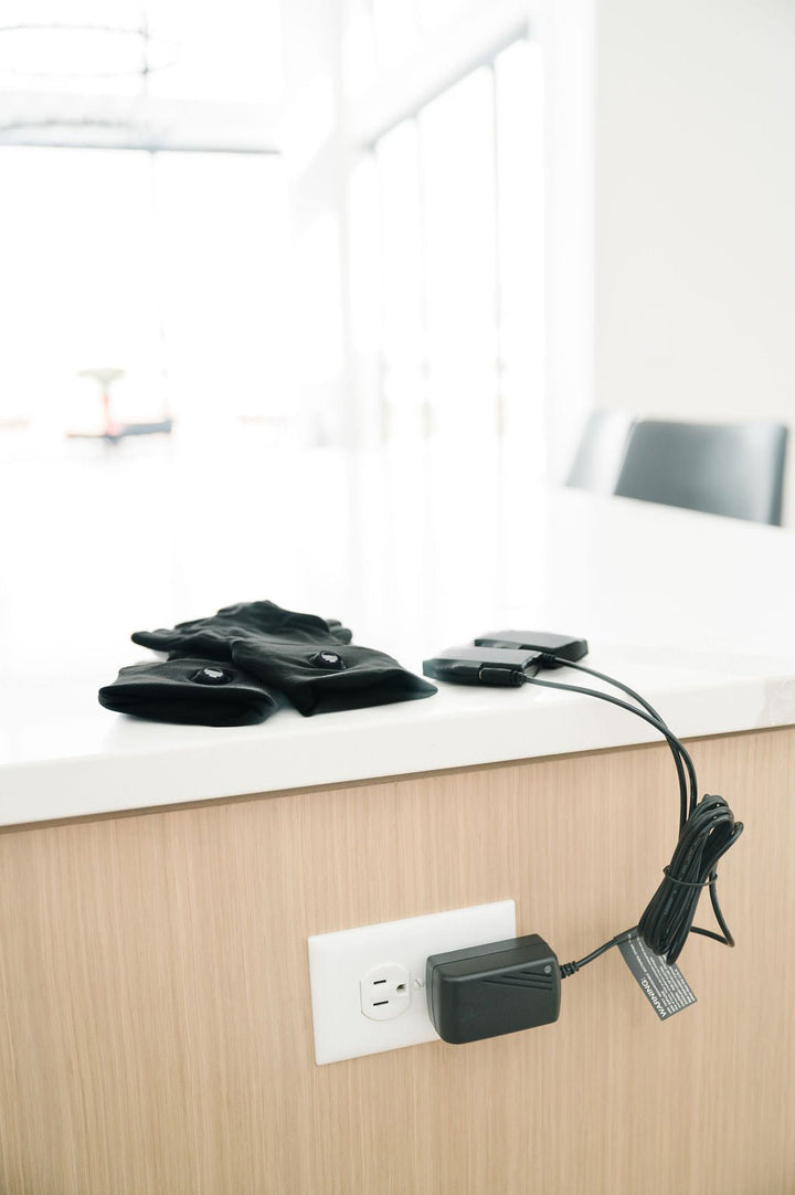 Toasty Touch heated gloves on a counter with 7V rechargeable batteries plugged into a wall charger